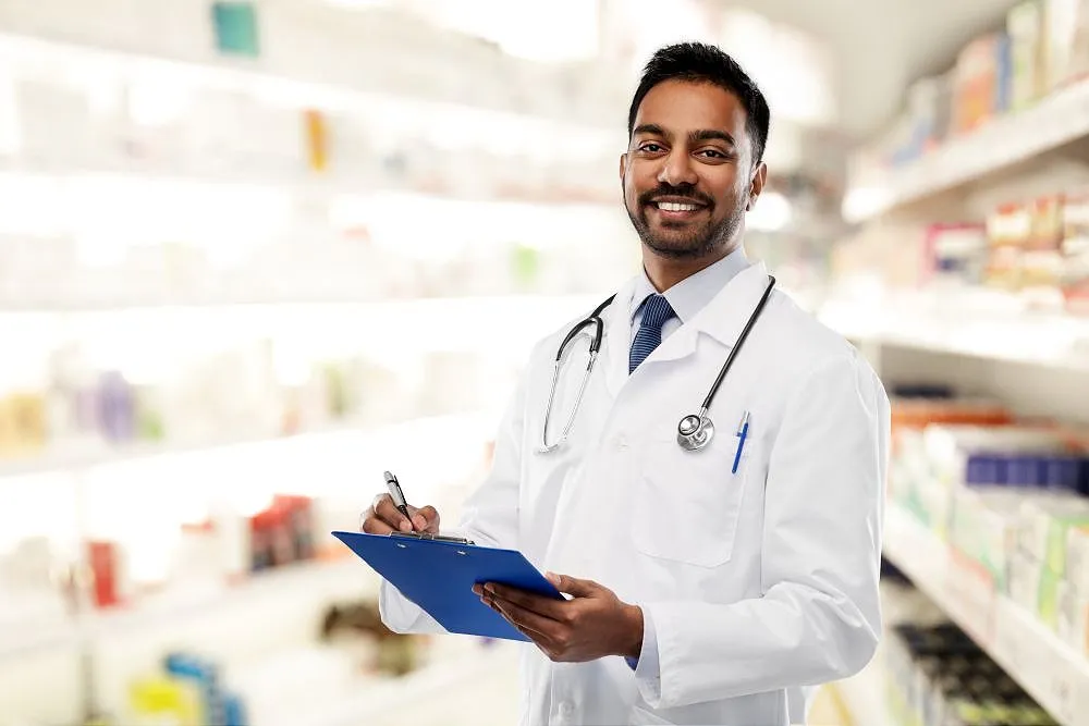 Pharmacist holding clipboard in pharmacy aisle smiling at camera